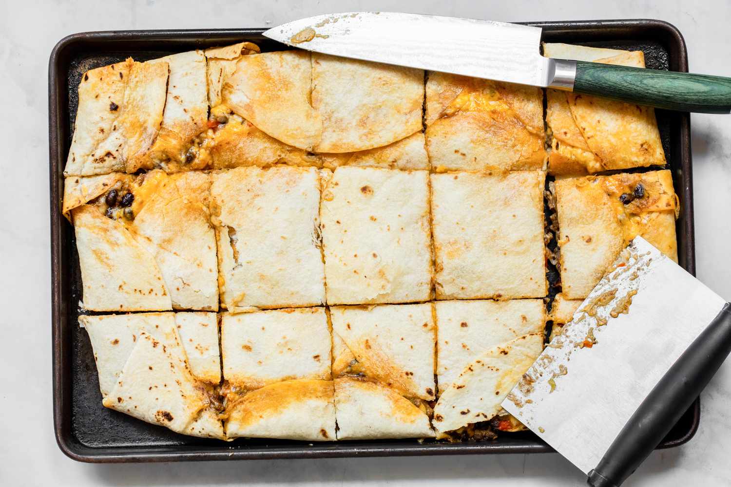 Tortillas, shredded cheese, cooked chicken, sliced bell peppers, sliced onions, salsa, and spices arranged on a clean kitchen counter in bright natural light