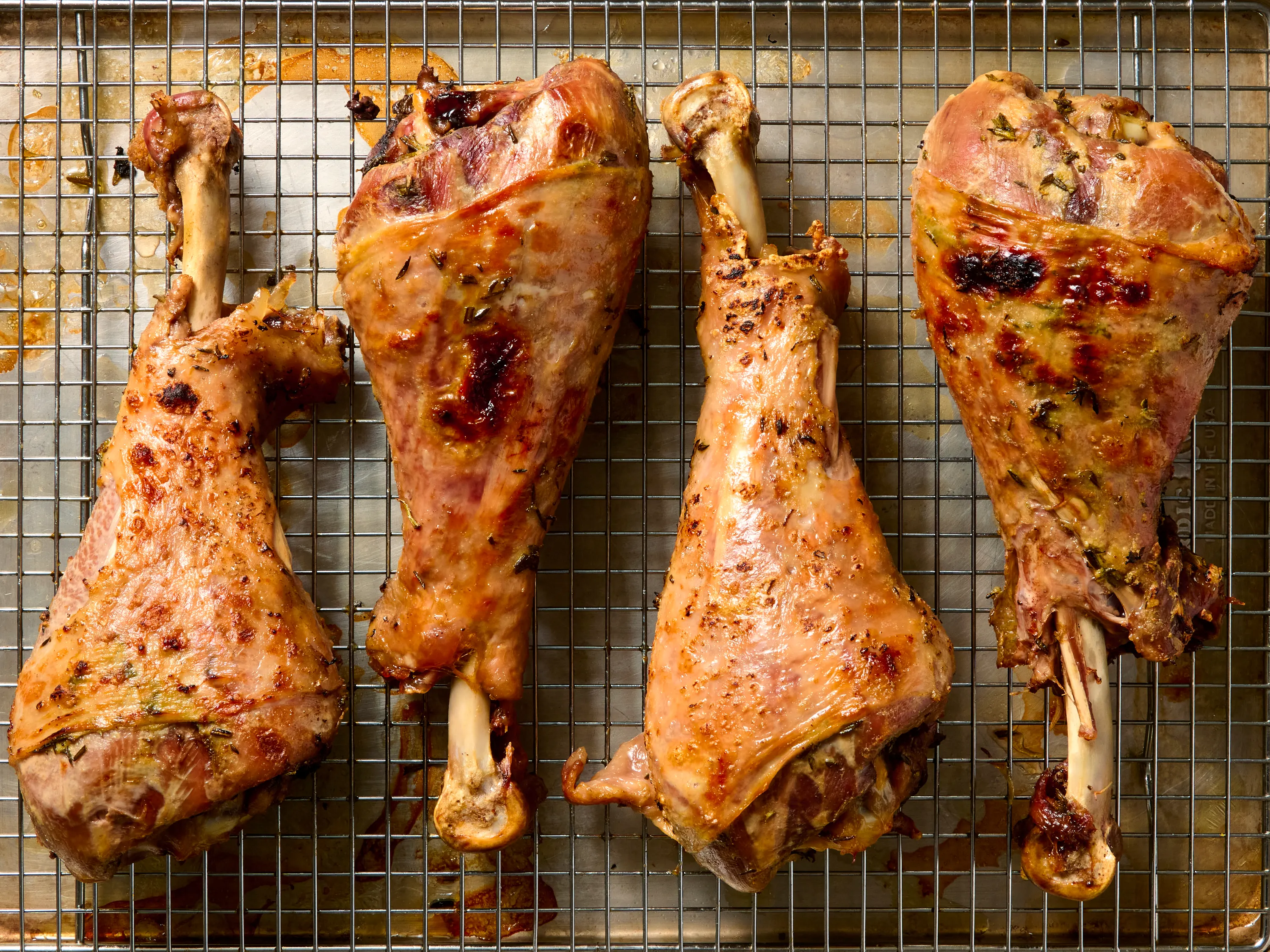 Turkey legs on a cutting board being sprinkled with a spice rub from a small bowl in a home kitchen