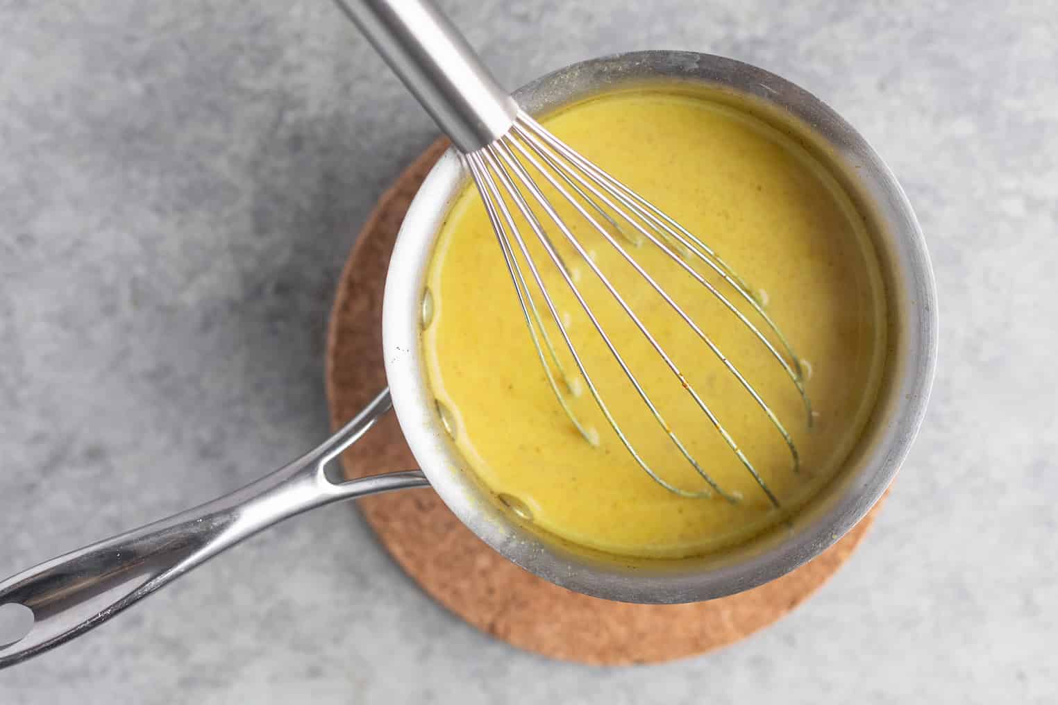 Turmeric and spices being whisked into milk in a small saucepan on a stovetop