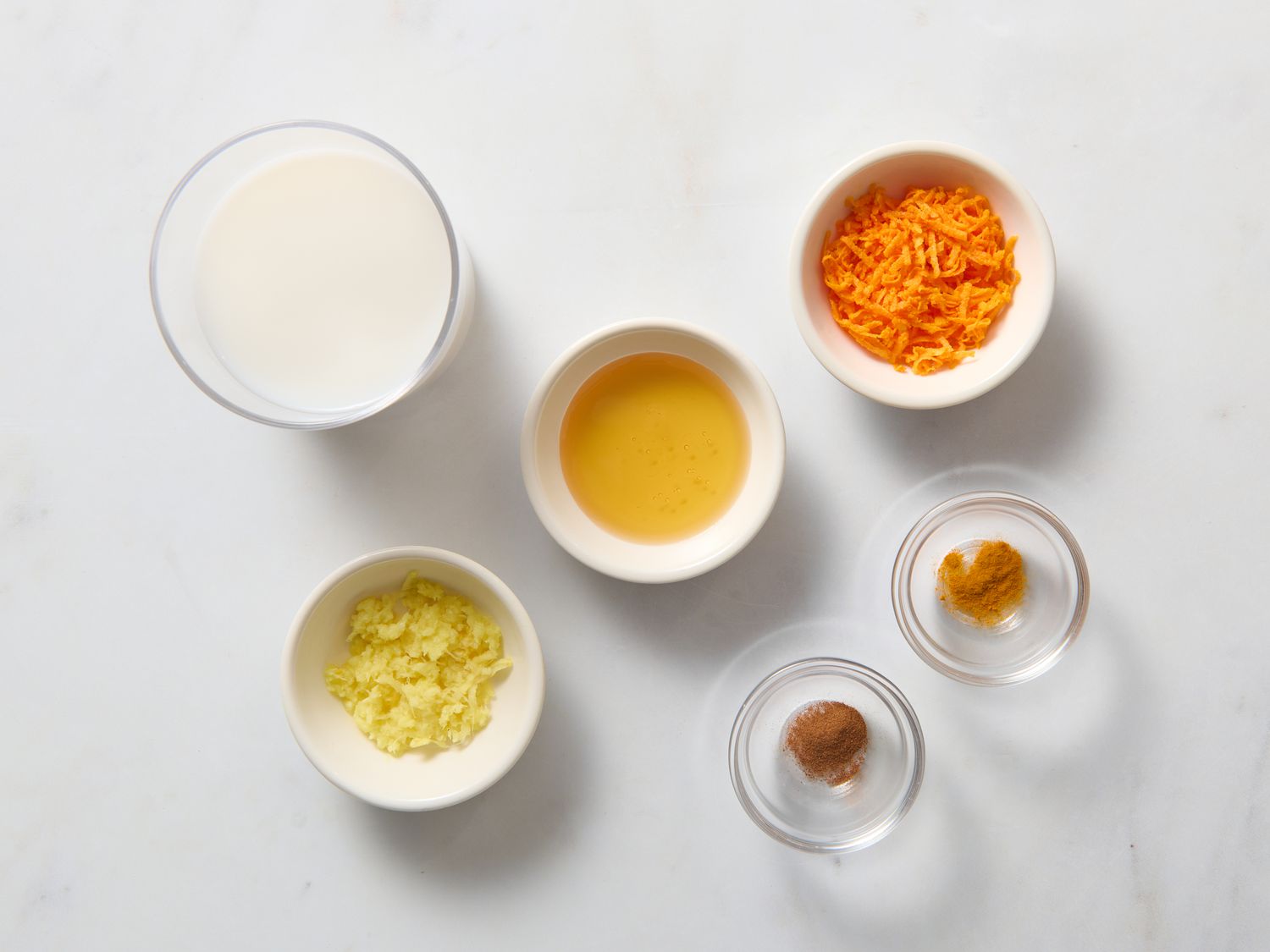 Turmeric, fresh ginger, cinnamon, black pepper, honey, and a small pitcher of milk arranged on a light kitchen counter
