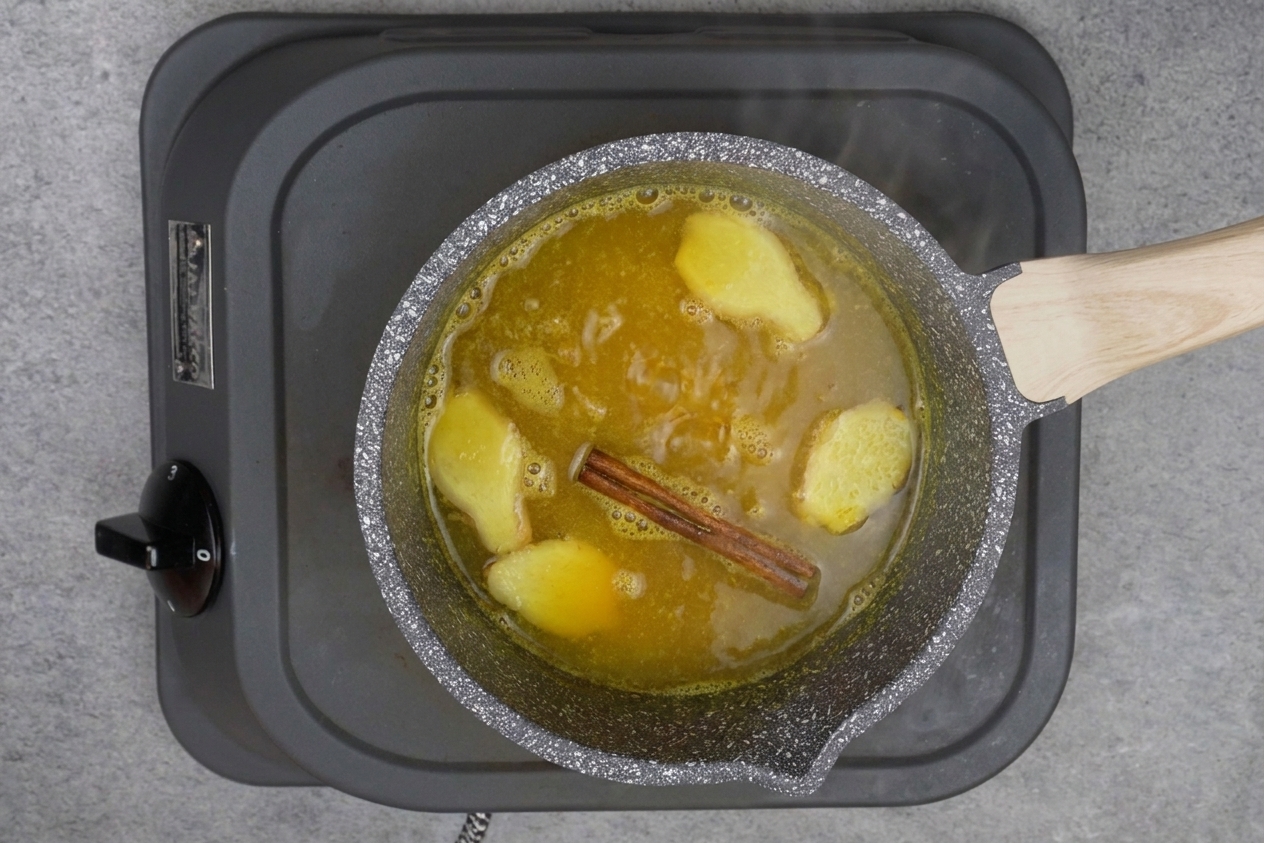 Turmeric tea simmering in a small saucepan on a stovetop, golden liquid with ginger slices visible