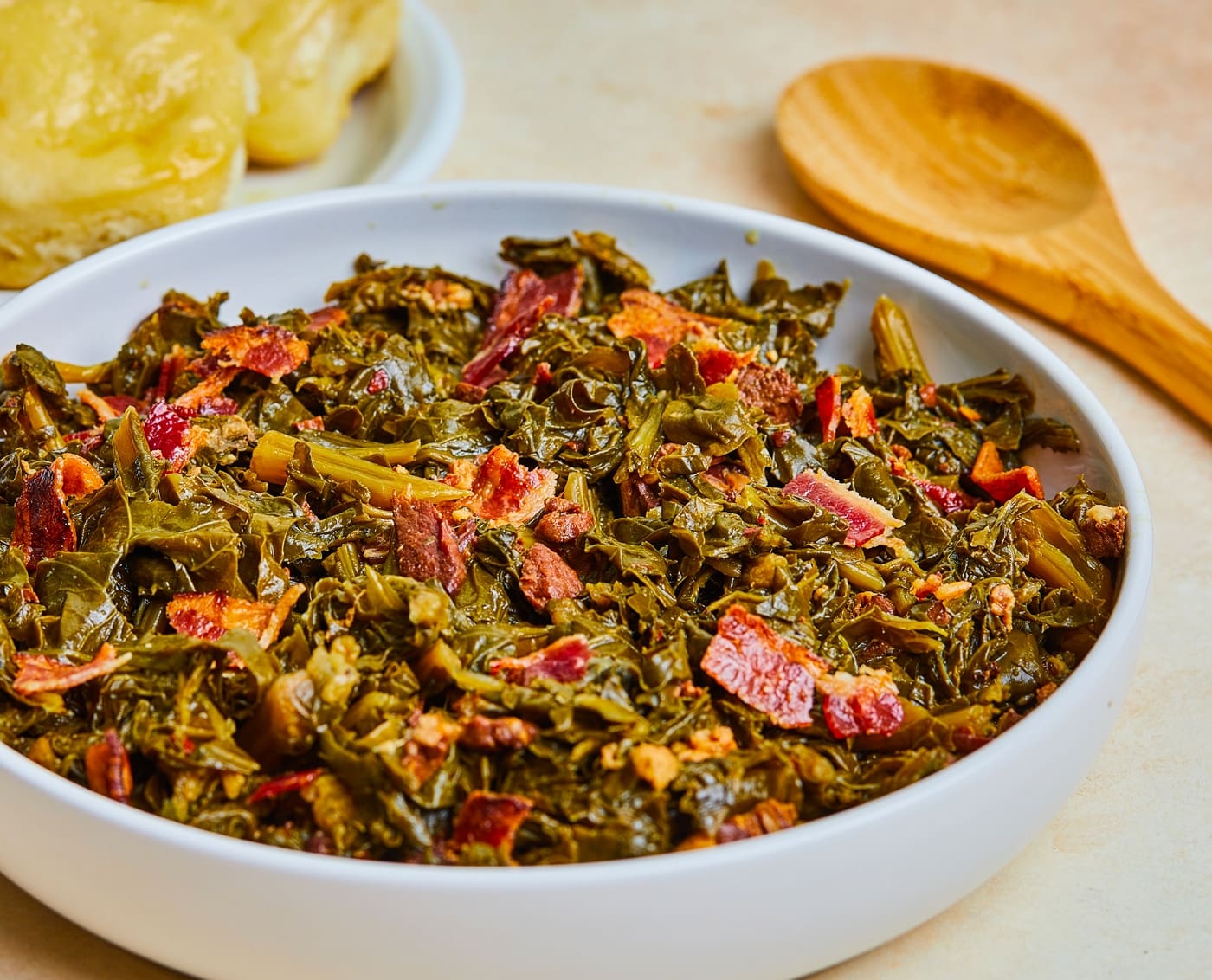 Turnip greens, chopped bacon, sliced onion, and minced garlic arranged on a cutting board beside a Dutch oven on a kitchen counter