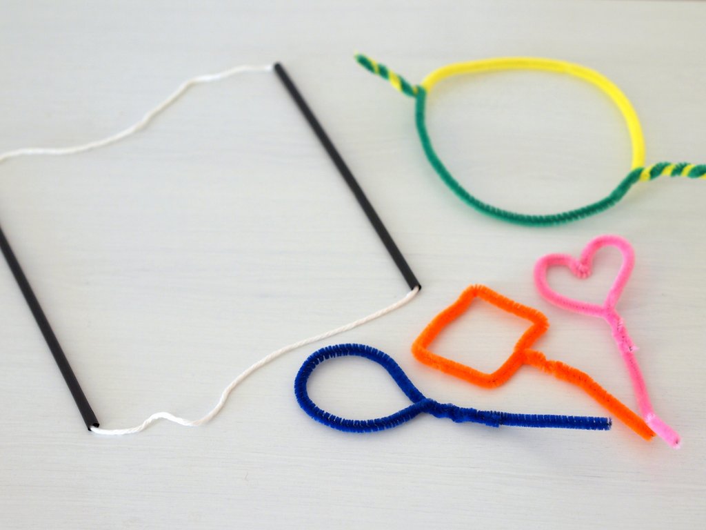 Two adult hands tying cotton string to two wooden dowels over a kitchen counter to make a simple giant bubble wand