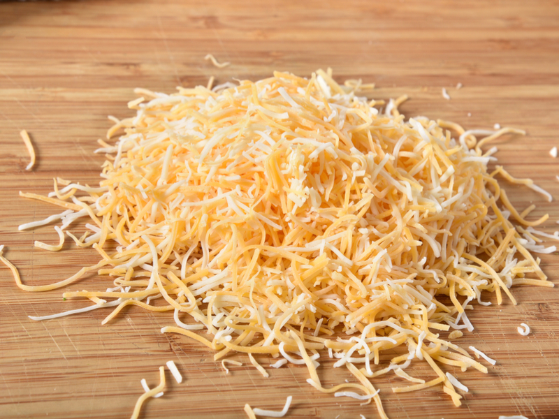 Two bowls of freshly shredded cheddar and Monterey Jack cheese next to a box grater