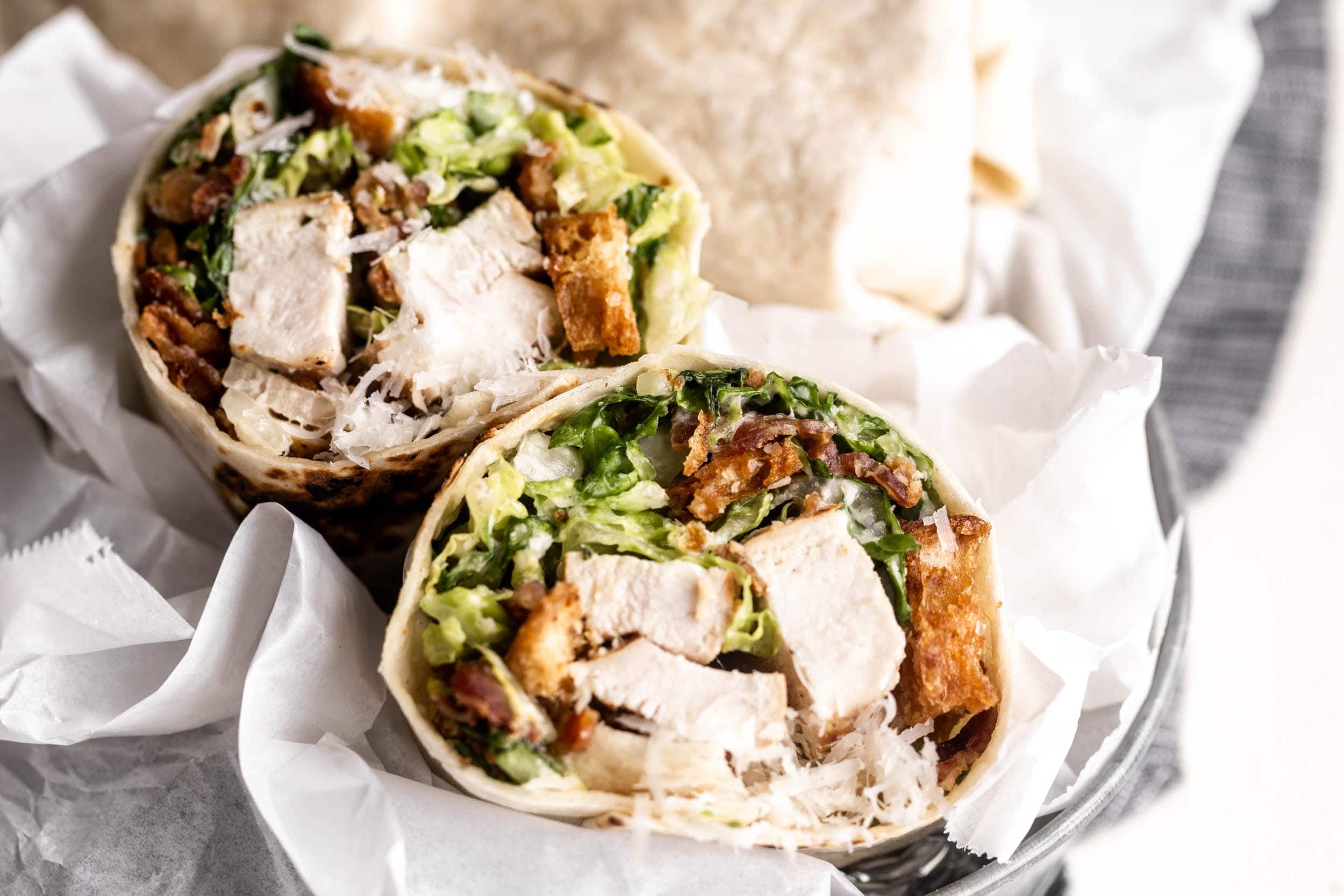 Two chicken Caesar wraps cut in half on a ceramic plate with lemon wedges and extra Parmesan on a sunlit kitchen table