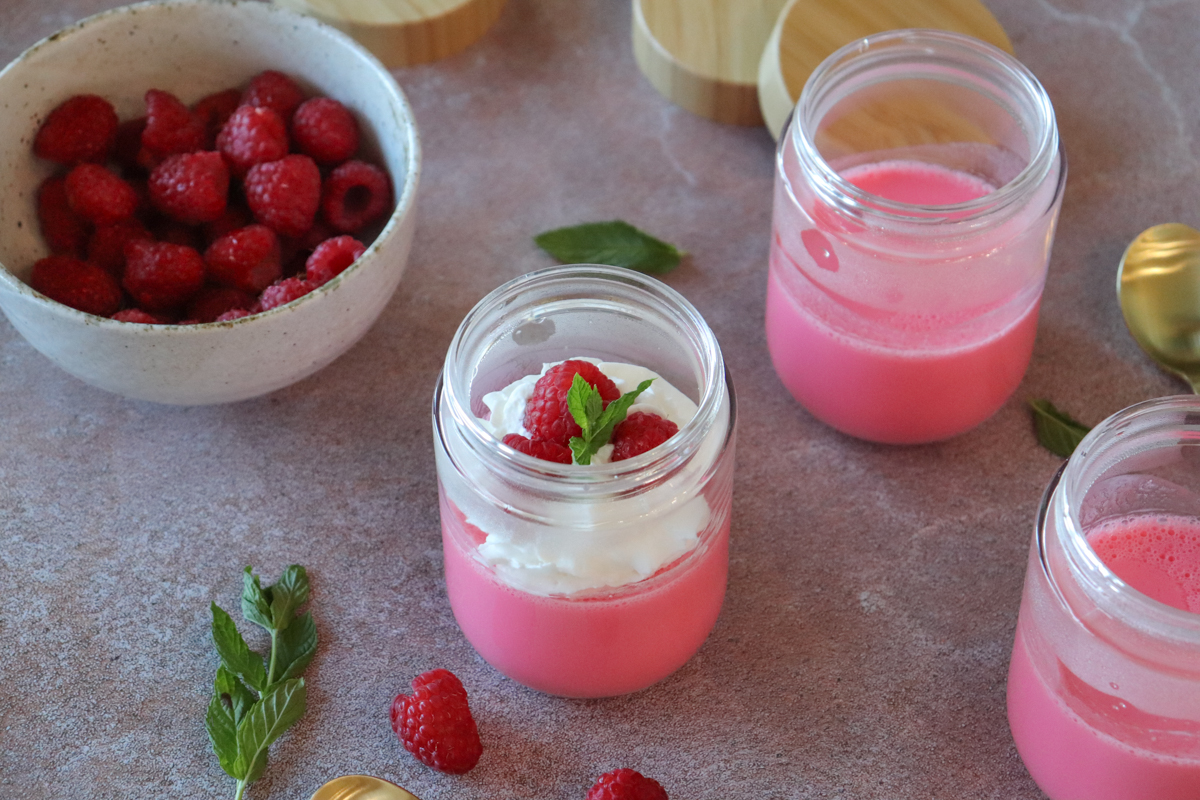 Two clear glass cups layered with bright red sugar-free gelatin, creamy Greek yogurt, and sliced strawberries on a light stone kitchen counter