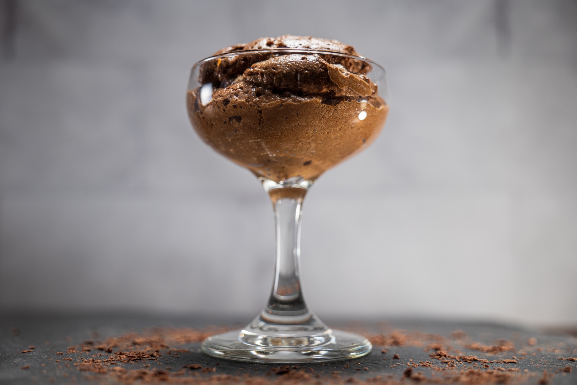 Two coupe glasses filled with dark chocolate mousse topped with a small dollop of whipped cream and chocolate shavings on a stone countertop with warm kitchen lighting