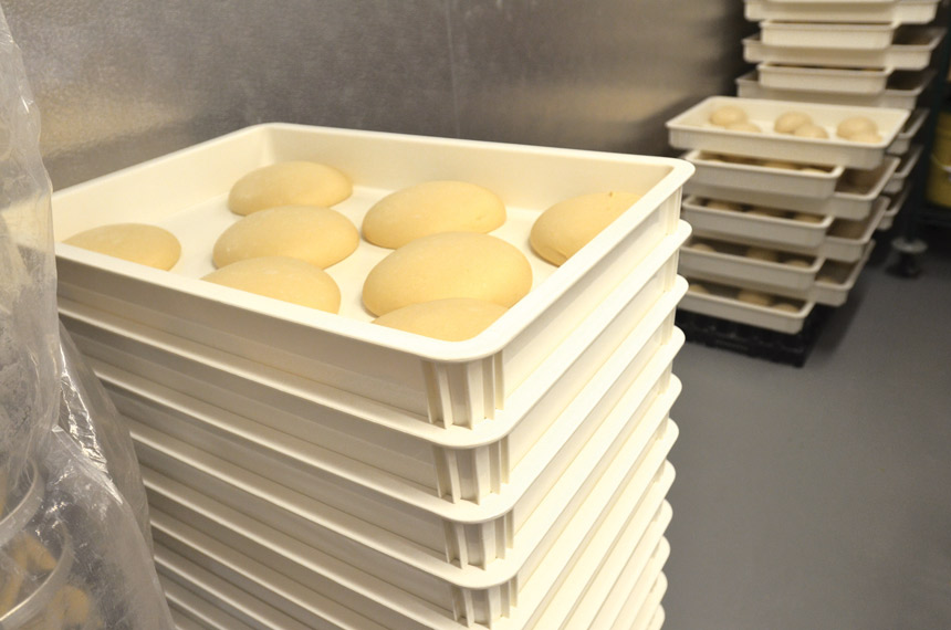 Two covered plastic dough containers holding risen pizza dough balls on a kitchen counter, showing how to store dough