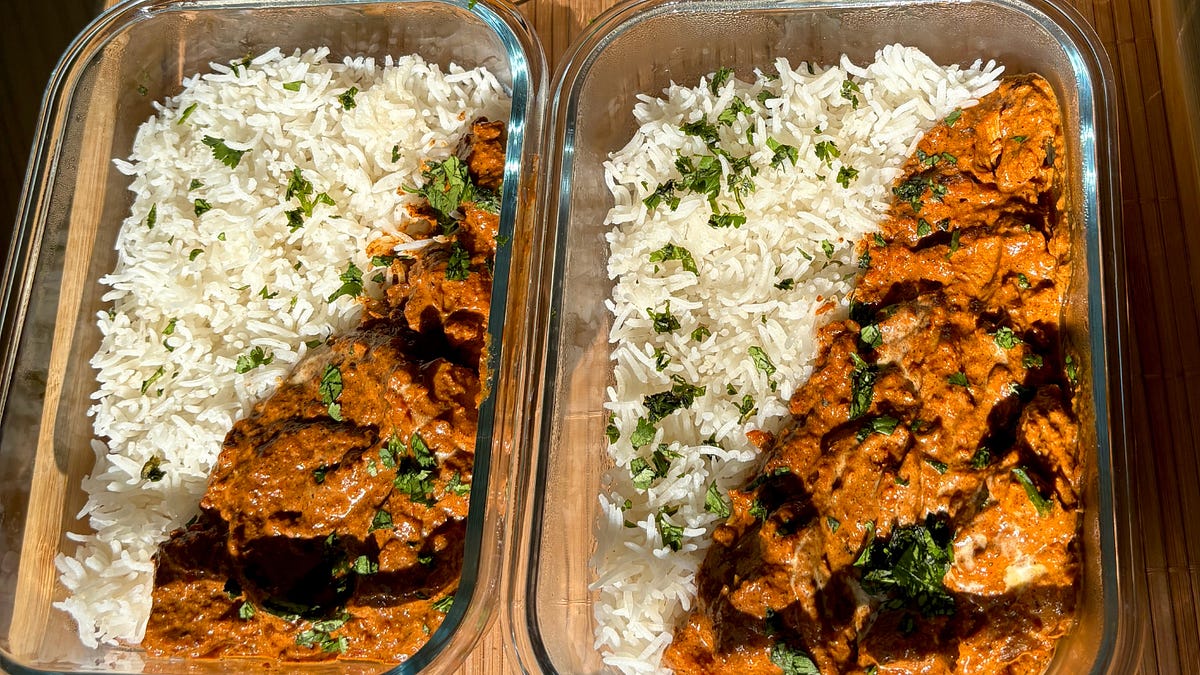Two glass meal prep containers filled with butter chicken and rice, lids off, on a tidy kitchen counter under warm light