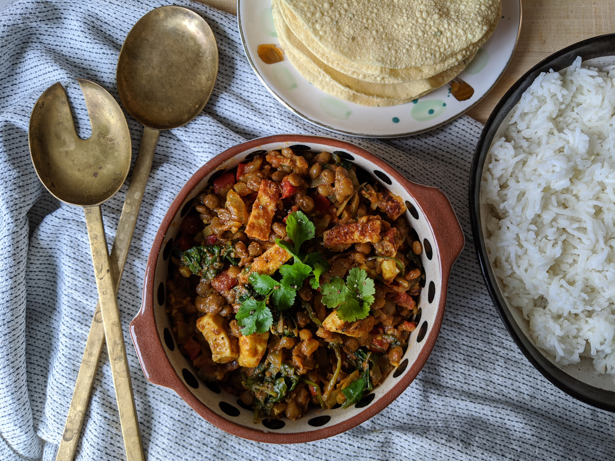 Two glass meal prep containers filled with orange curry sauce and paneer cubes, lids off on a kitchen counter