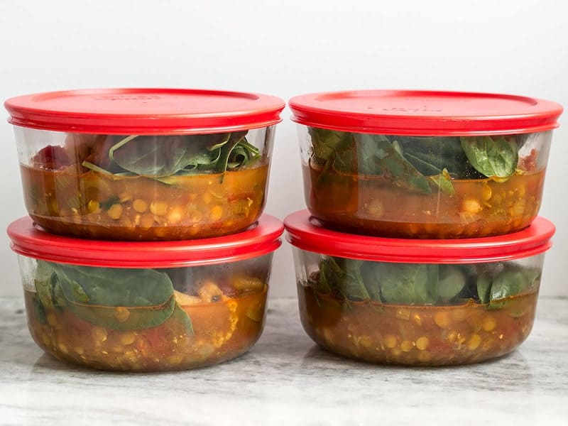 Two glass meal prep containers filled with red lentil stew on a kitchen counter, lids nearby, ready for the refrigerator