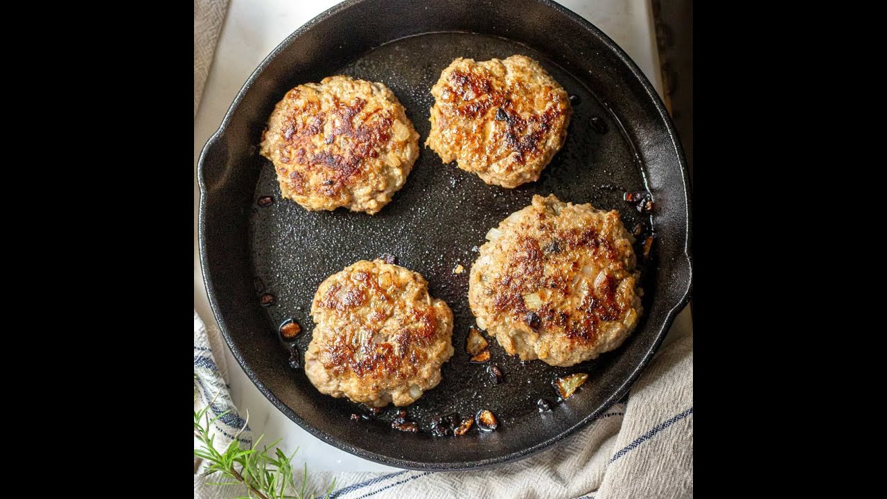 Two golden-brown turkey burger patties in a cast iron skillet with a few toasted buns nearby on a warm kitchen counter