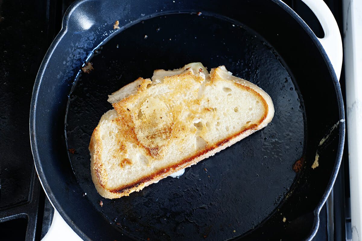 Two grilled cheese sandwiches cooking in a skillet as the first side turns golden brown