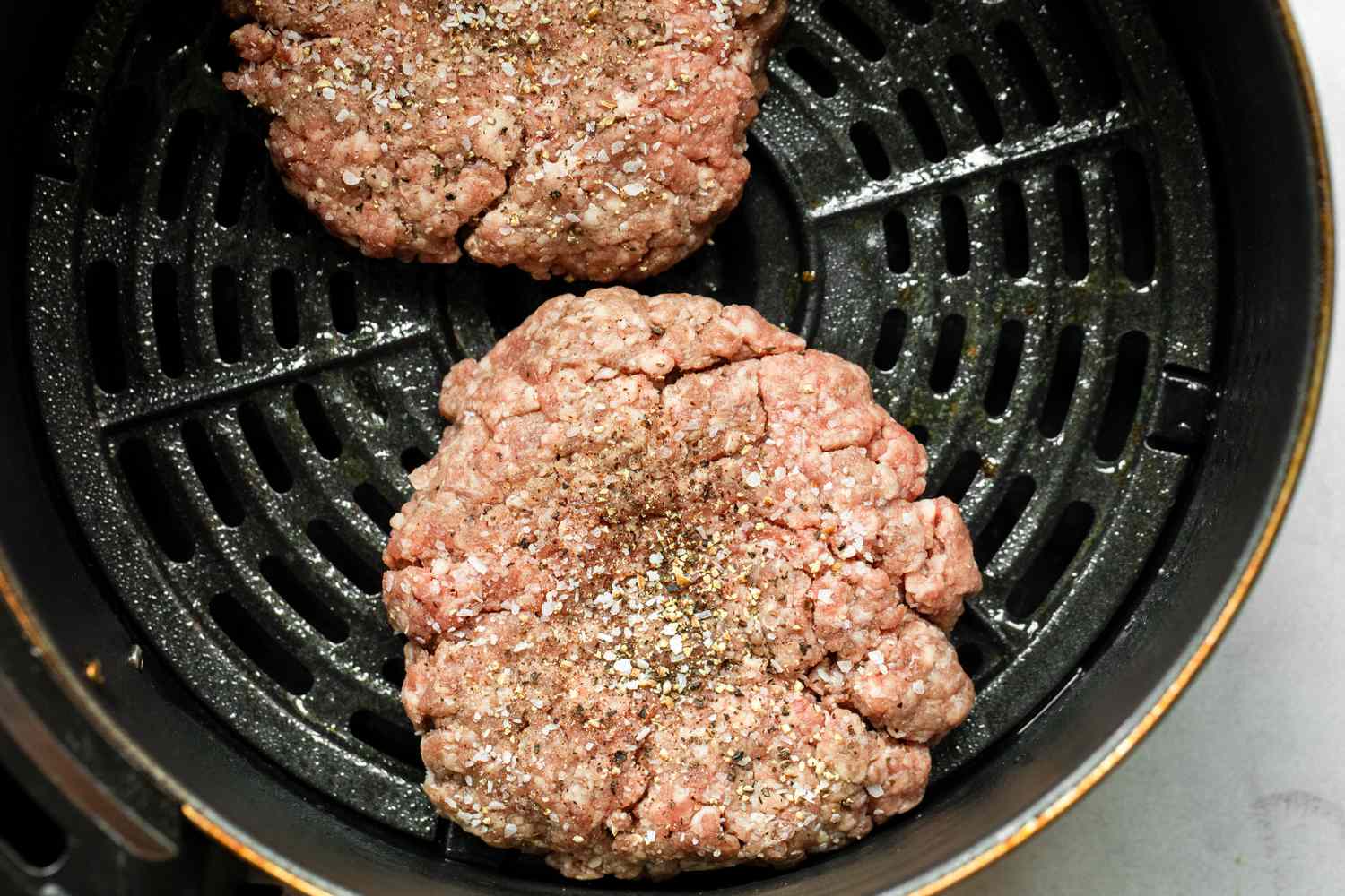 Two juicy hamburger patties in an air fryer basket with browned, crisp edges and a light sheen of rendered fat