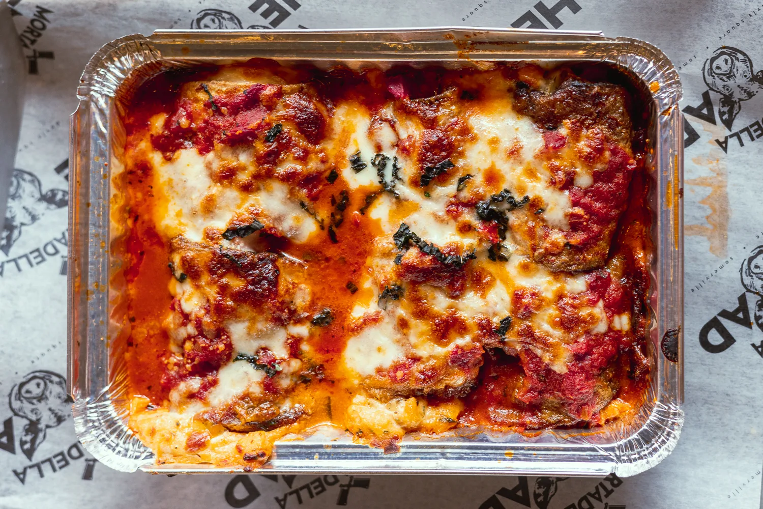 Two leftover slices of eggplant lasagna in a glass meal prep container with a snapped-on lid on a kitchen counter