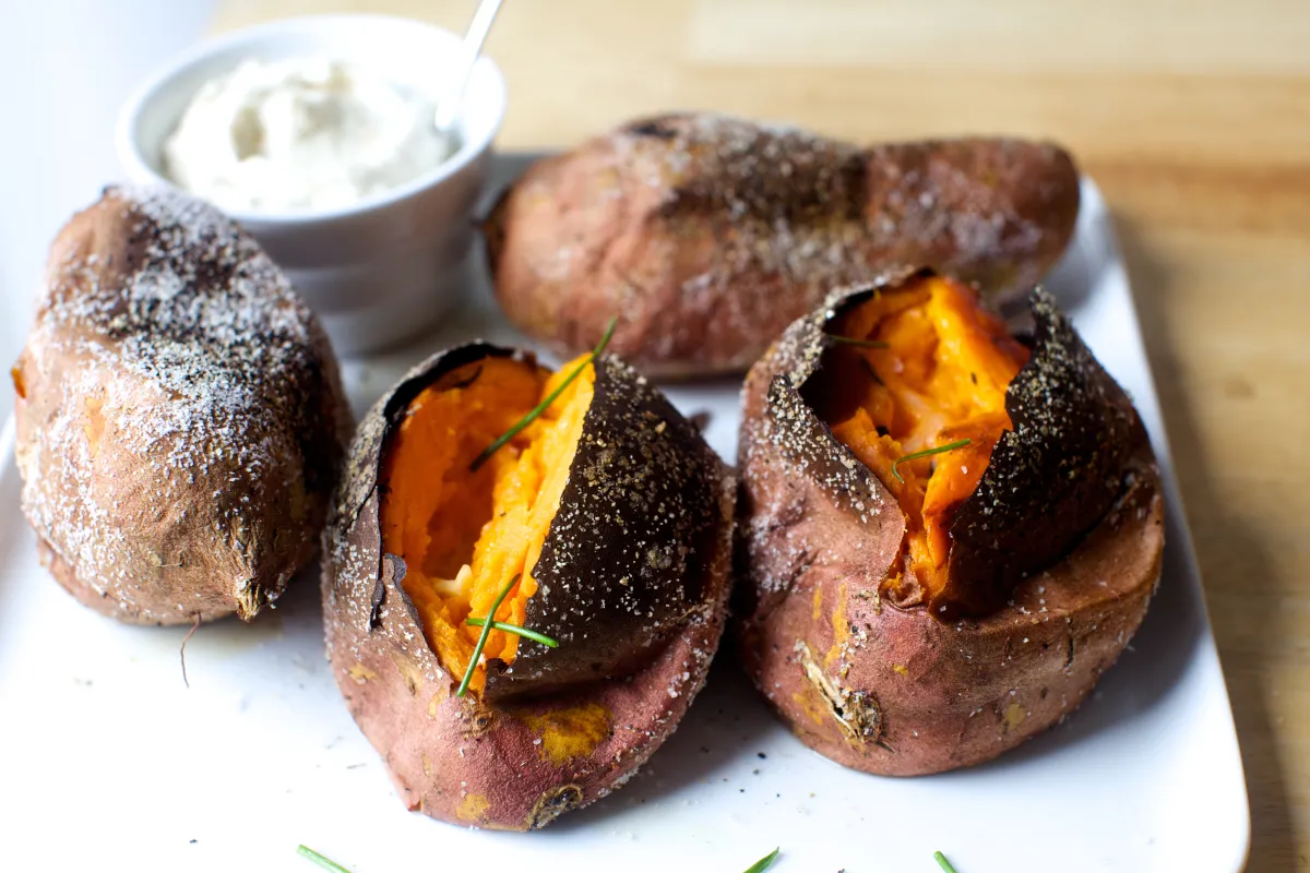 Two roasted sweet potatoes split open on a parchment-lined baking sheet with caramelized edges on a bright kitchen counter