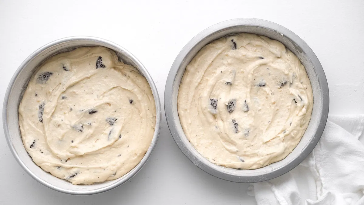 Two round cake pans filled with chocolate Oreo cake batter on a kitchen counter, ready to go into the oven