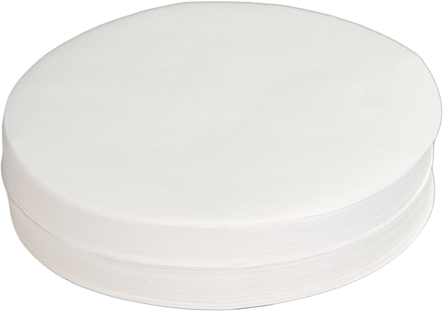 Two round cake pans greased and lined with parchment circles on a kitchen counter, ready for batter