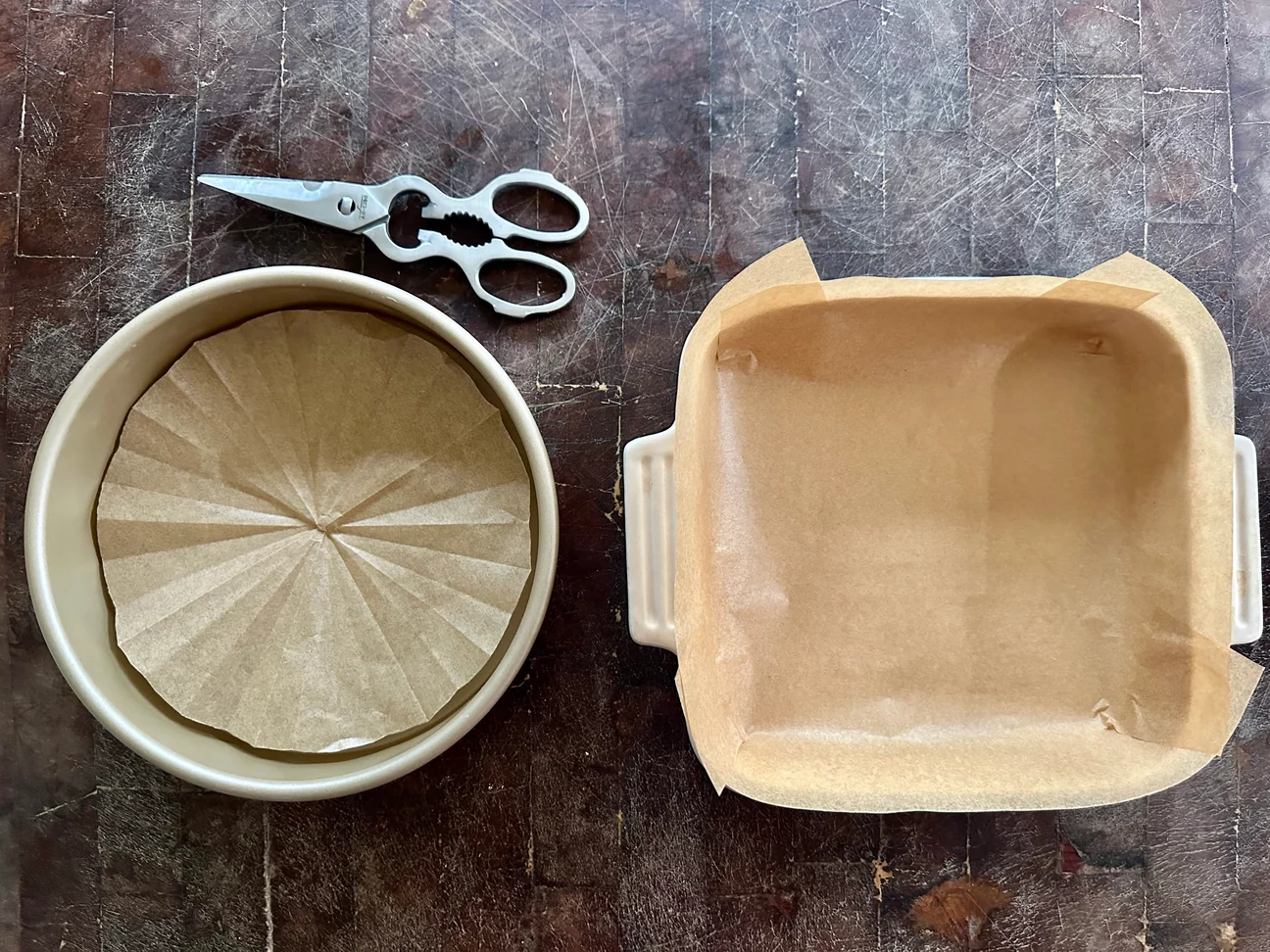 Two round cake pans lined with parchment paper on a clean countertop, ready for batter
