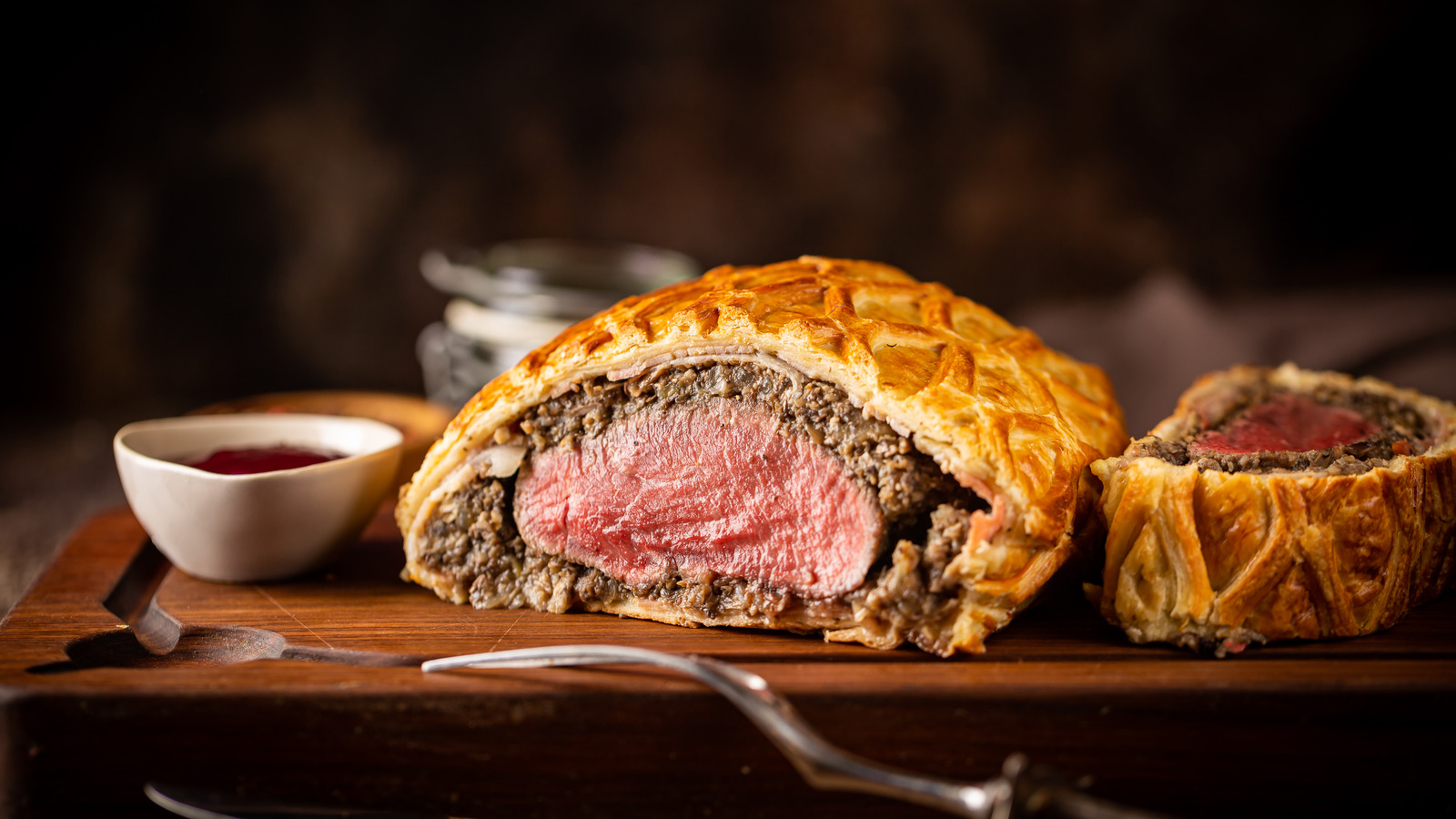 Two slices of beef Wellington stored in a glass container with a tight lid on a kitchen counter, showing flaky pastry and the mushroom layer