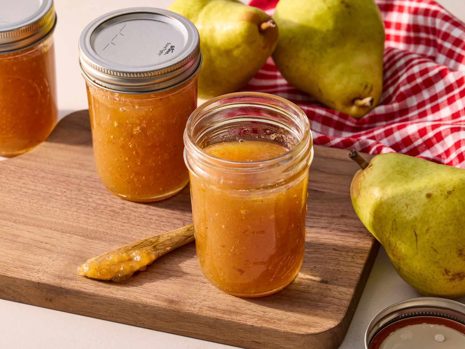 Two small glass jars of pear butter with lids on, cooling on a kitchen towel on a countertop