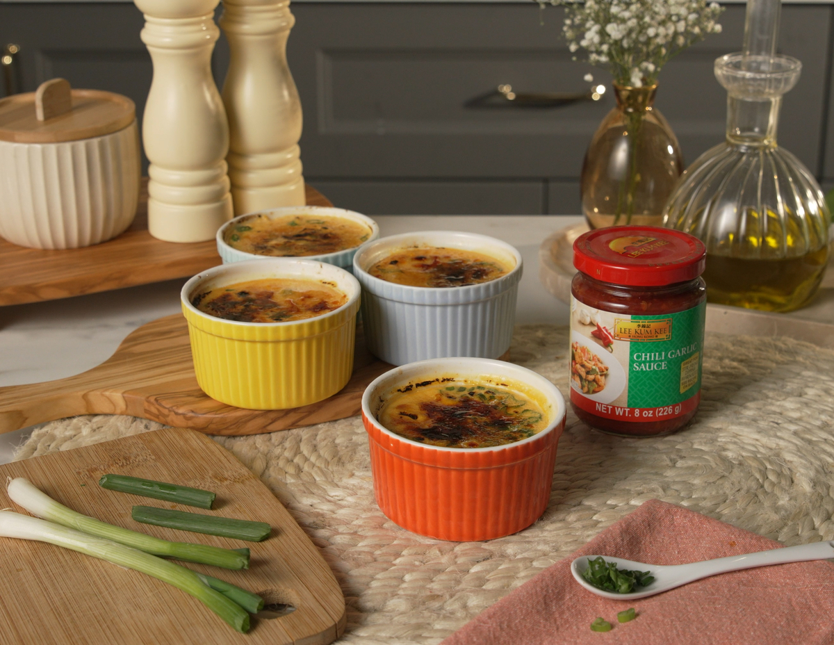 Two small ramekins of savory crab brûlée on a wooden table, each topped with a blistered, crackly golden Parmesan crust, with lemon wedges and a folded napkin nearby