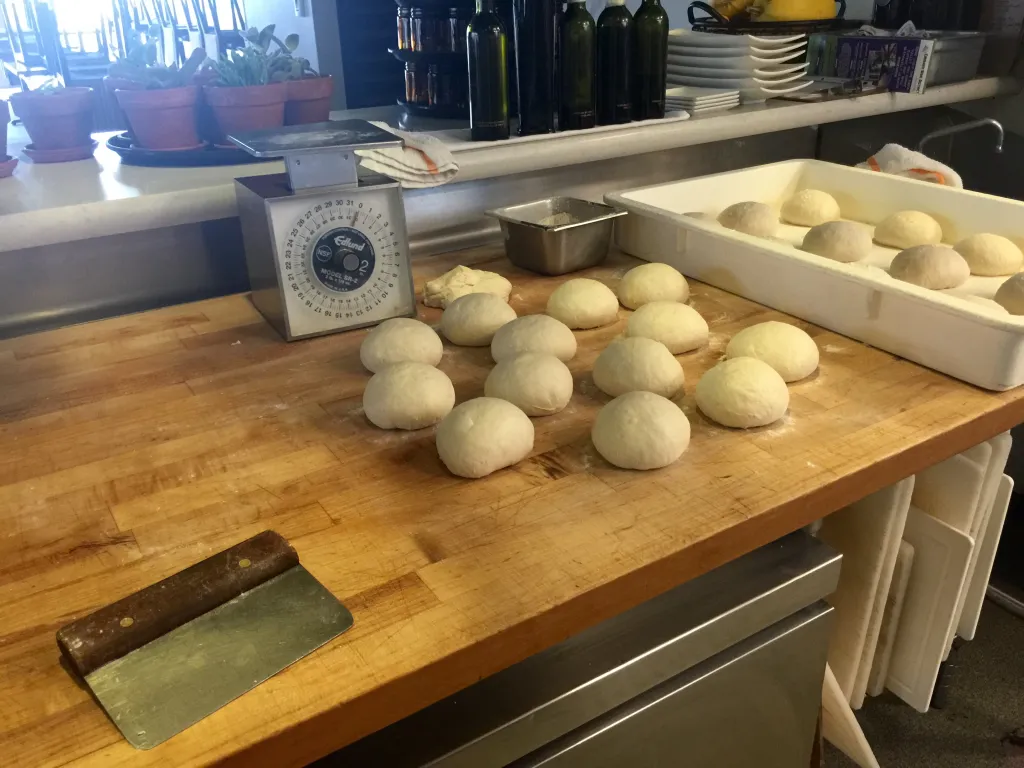 Two smooth pizza dough balls resting on a lightly floured countertop under a clean kitchen towel