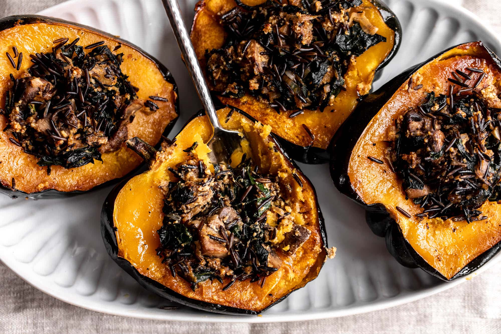 Two stuffed acorn squash halves in a glass meal prep container with a snap-on lid on a kitchen counter, ready for refrigeration