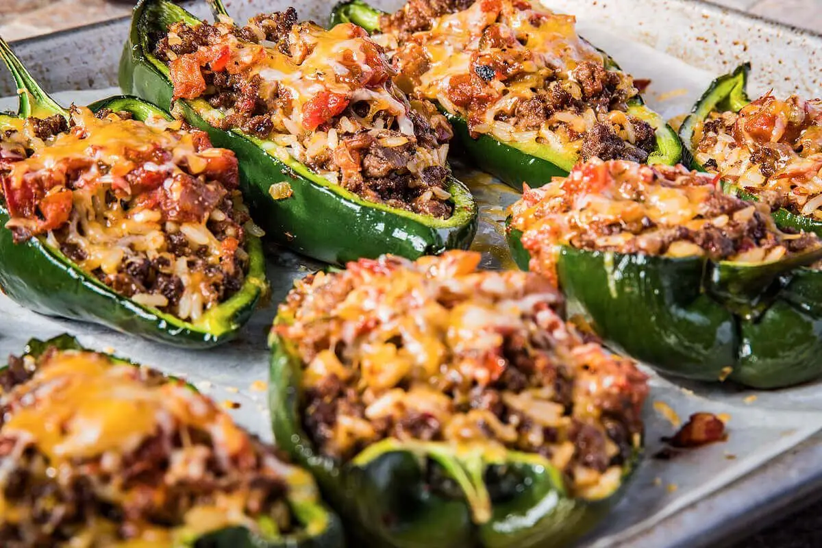 Two stuffed poblano pepper halves in a glass meal prep container with a spoonful of sauce, set on a kitchen counter