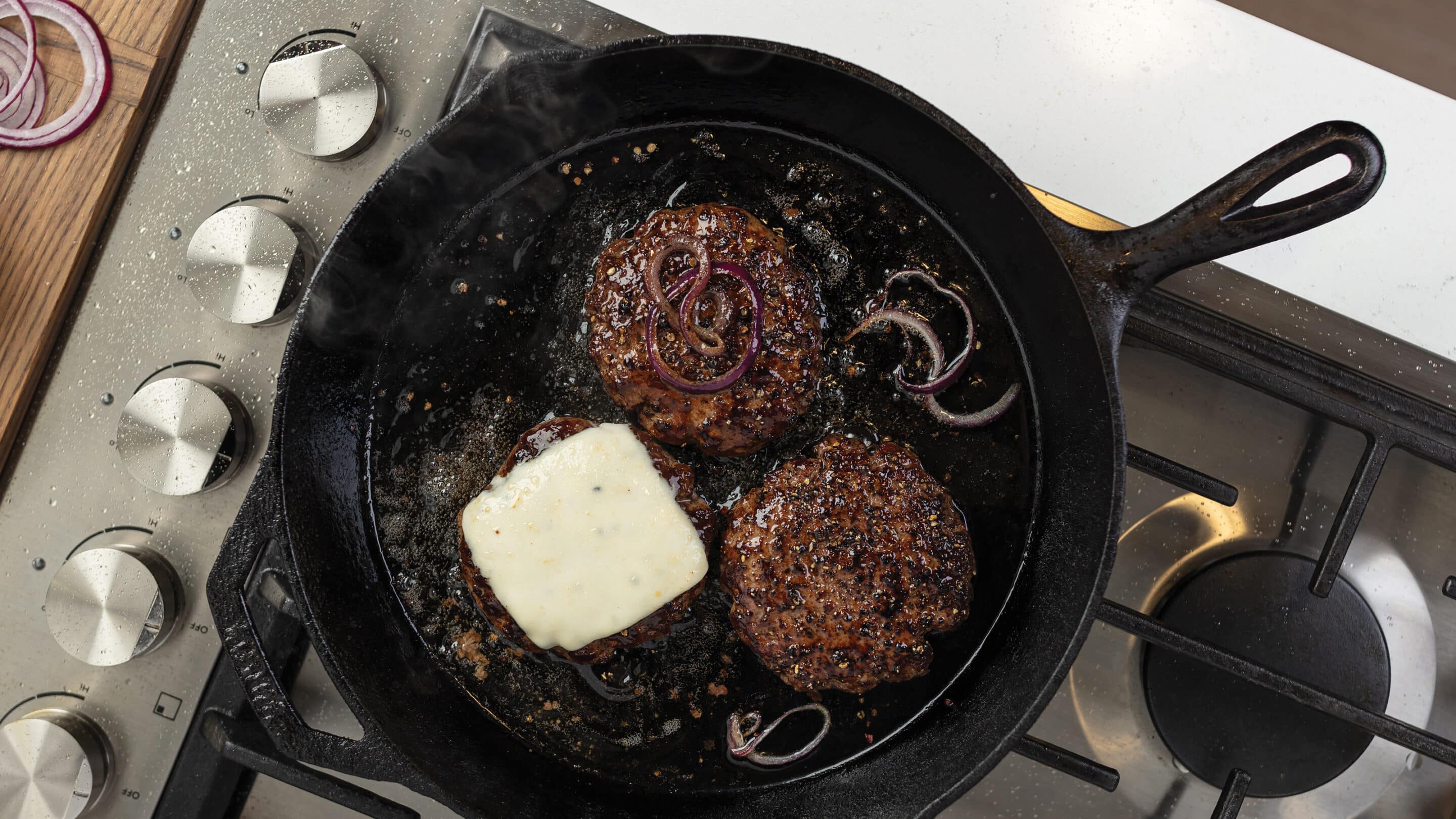 Two thin smash burger patties sizzling in a cast iron skillet with browned lacy edges forming
