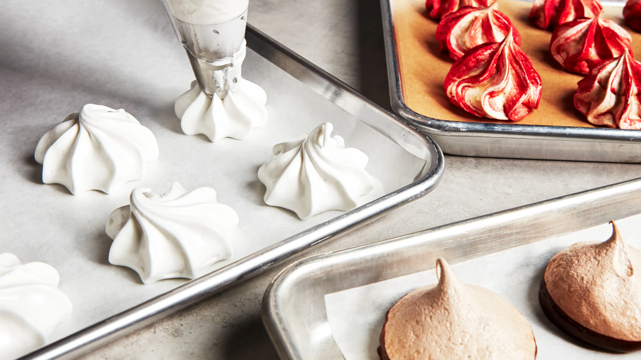 Unbaked meringue cookie swirls piped onto parchment paper on a metal sheet pan, ready to go into the oven