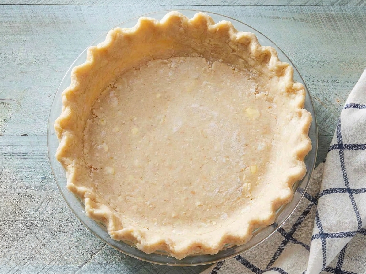 Unbaked pie crust fitted into a glass pie dish on a countertop, edges lightly crimped
