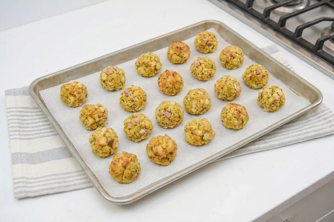 Unbaked stuffing balls arranged on a parchment-lined baking sheet on a kitchen counter, ready to go into the oven