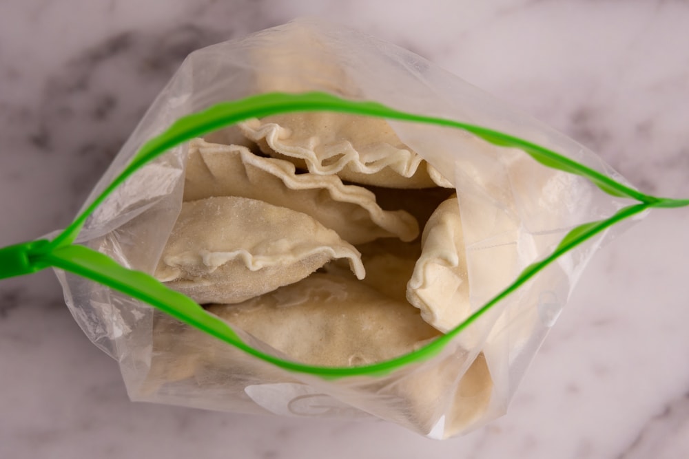 Uncooked perogies arranged in a single layer on a parchment-lined baking sheet ready to be frozen, on a tidy kitchen counter