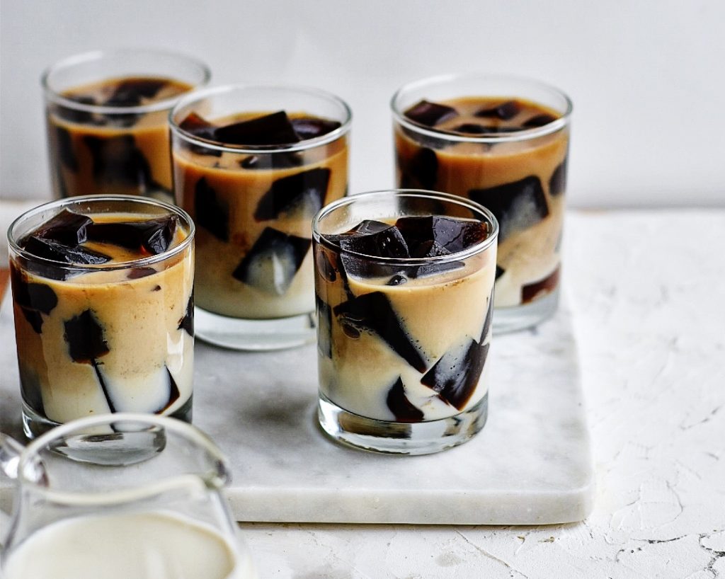 Unflavored gelatin packets, a bowl of sugar, a measuring cup of strong brewed coffee, and a small pitcher of cream arranged on a tidy kitchen counter