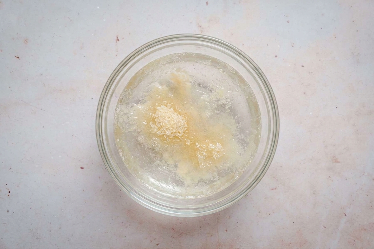 Unflavored gelatin sprinkled over cold water in a small bowl, blooming on a kitchen counter