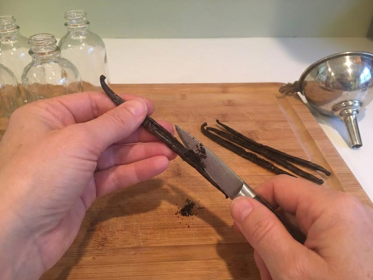 Vanilla beans being split lengthwise on a wooden cutting board with a paring knife, showing the seeds inside