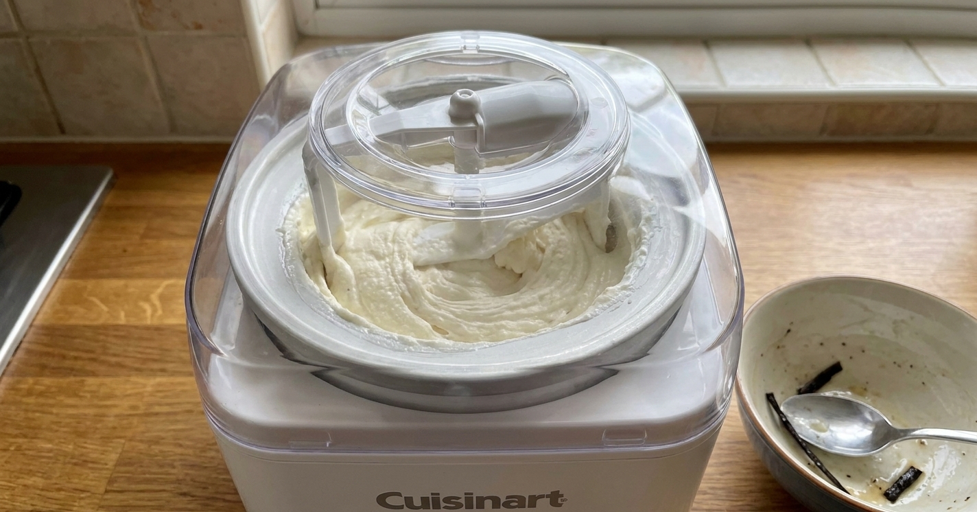 Vanilla ice cream base churning inside a Cuisinart ice cream maker with the lid on and the machine running on a bright kitchen counter