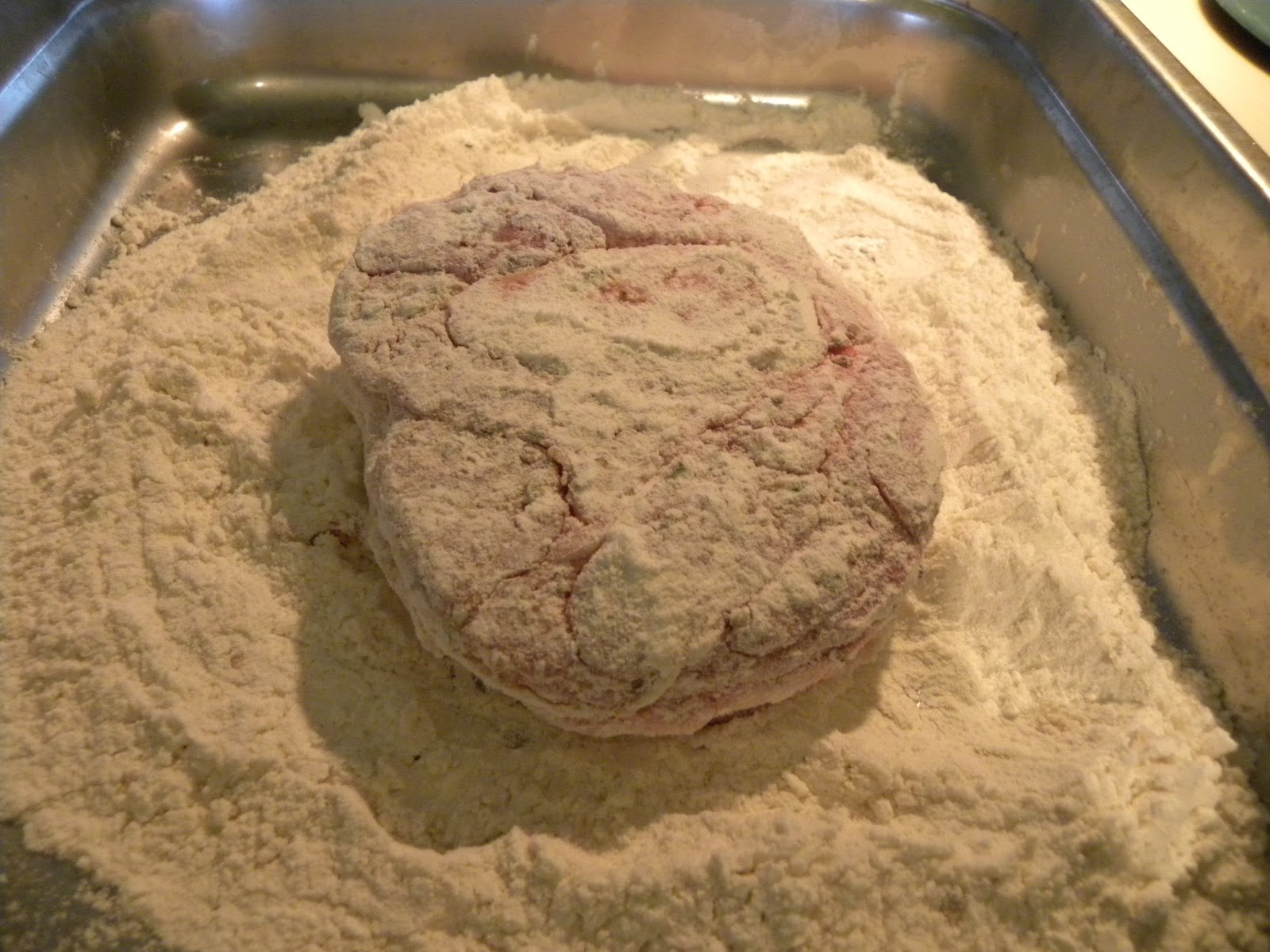 Veal shanks being lightly dredged in flour on a kitchen counter with a shallow dish and a dusting of flour