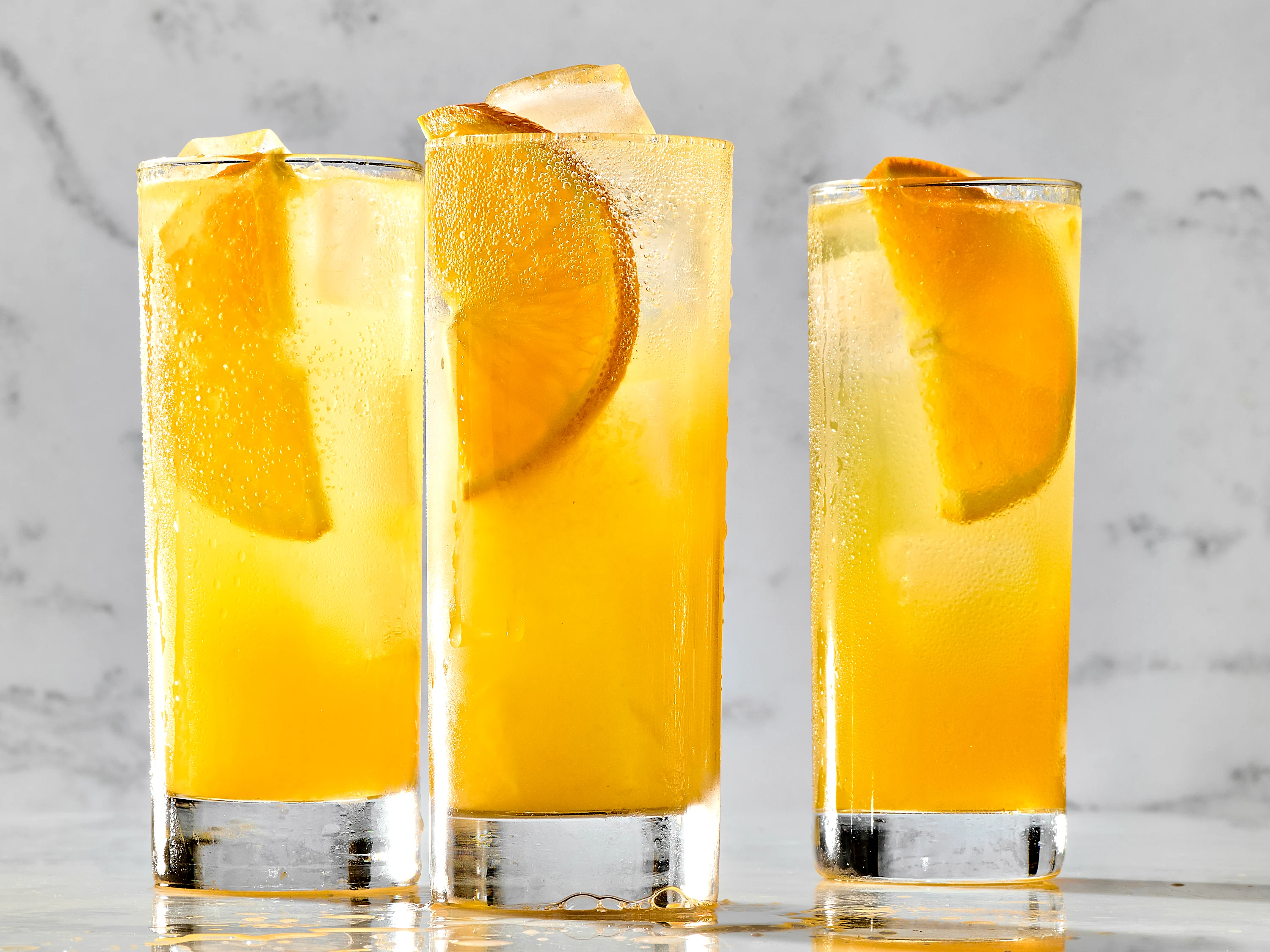 Vodka, a small pitcher of orange juice, a whole orange, and a jigger arranged on a bright kitchen counter