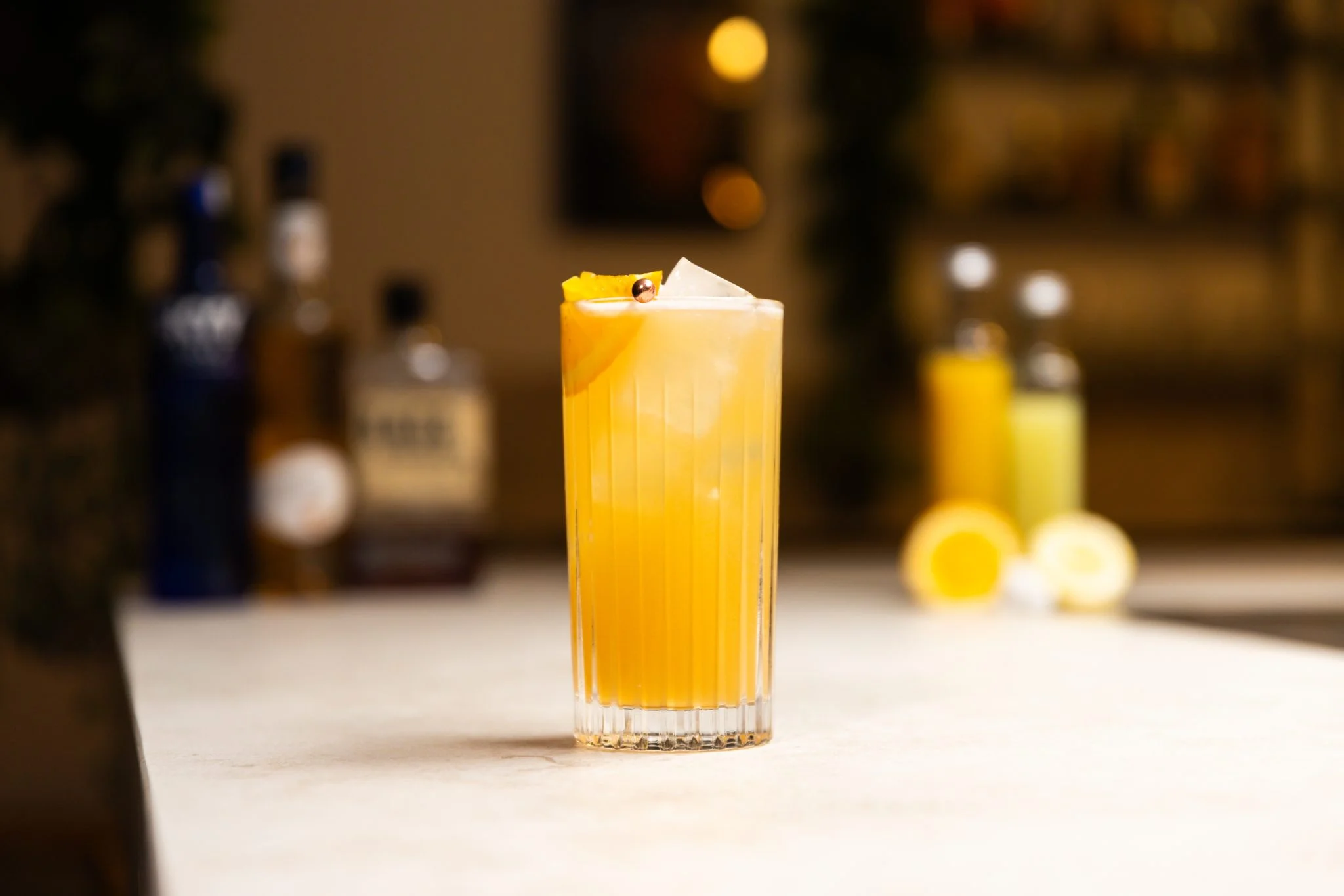 Vodka, peach schnapps, sour mix, and lemon-lime soda arranged on a clean kitchen counter beside a jigger and cocktail shaker.
