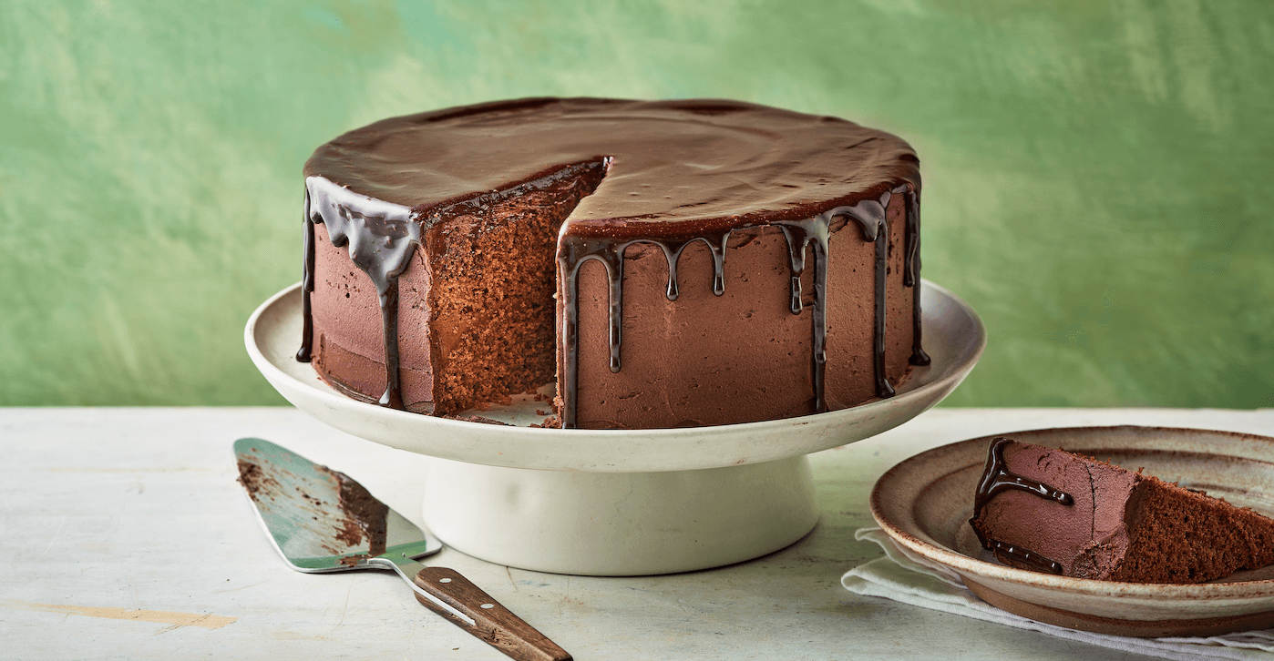 Warm chocolate ganache being poured over a cake on a cooling rack, glossy and smooth