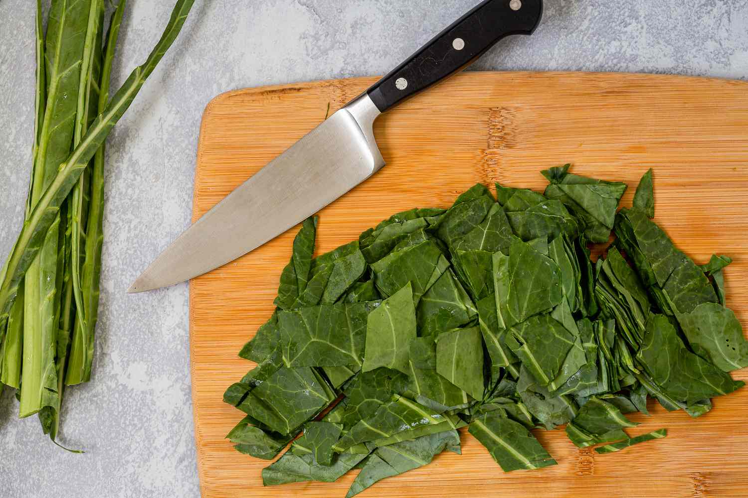 Washed turnip greens piled on a cutting board with the leaves sliced into ribbons and thick stems set aside, kitchen counter in warm light