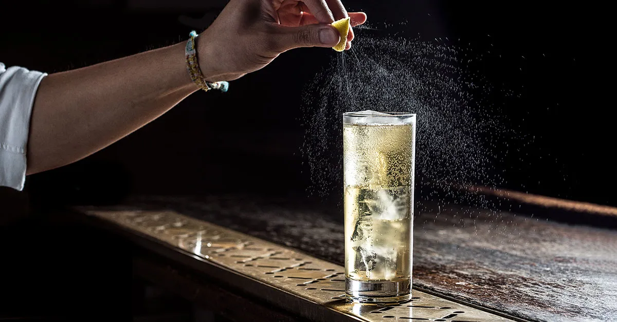 Whiskey, sparkling water, a lemon, a jigger, and large ice cubes arranged on a tidy kitchen counter, ready to make a highball