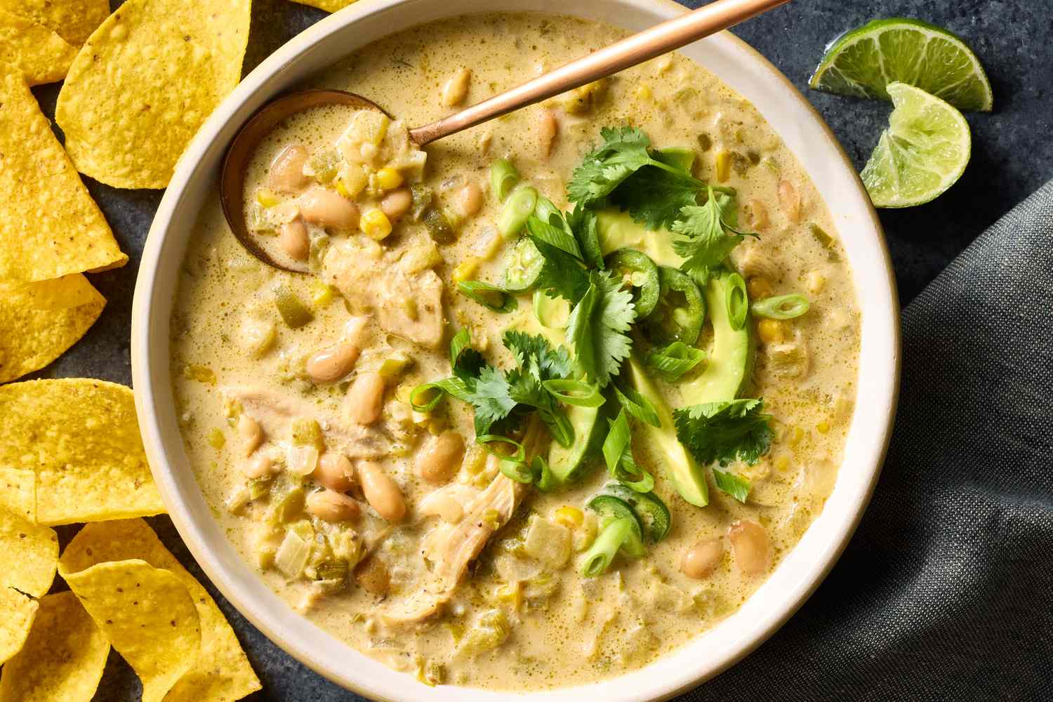 White chicken chili simmering in a slow cooker with a wooden spoon stirring the creamy broth with visible beans and shredded chicken