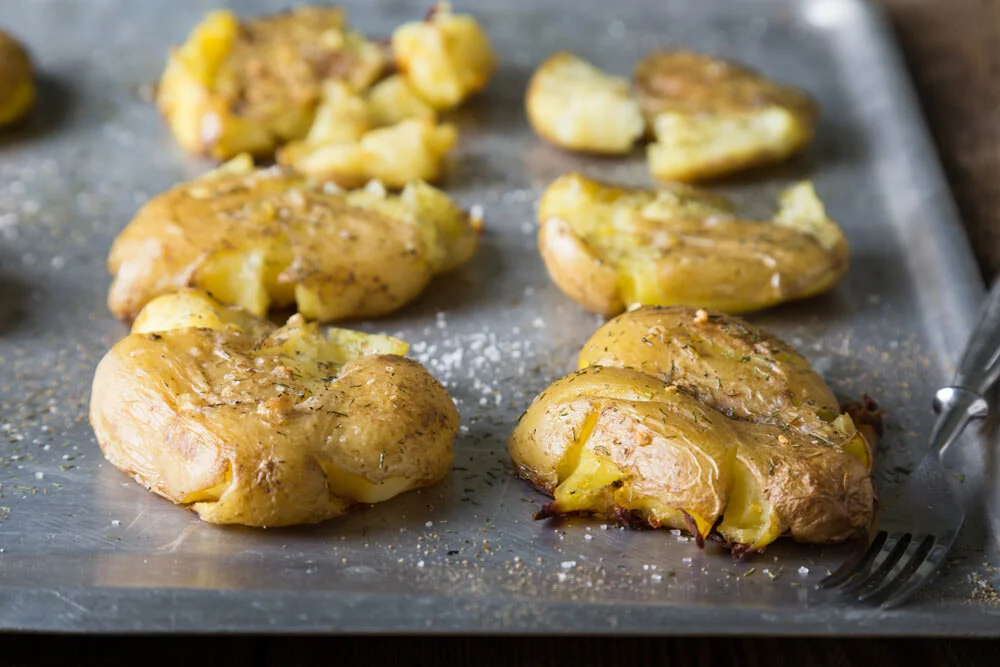 Whole Yukon Gold potatoes, a small bowl of olive oil, garlic, rosemary, kosher salt, and black pepper arranged on a bright kitchen counter