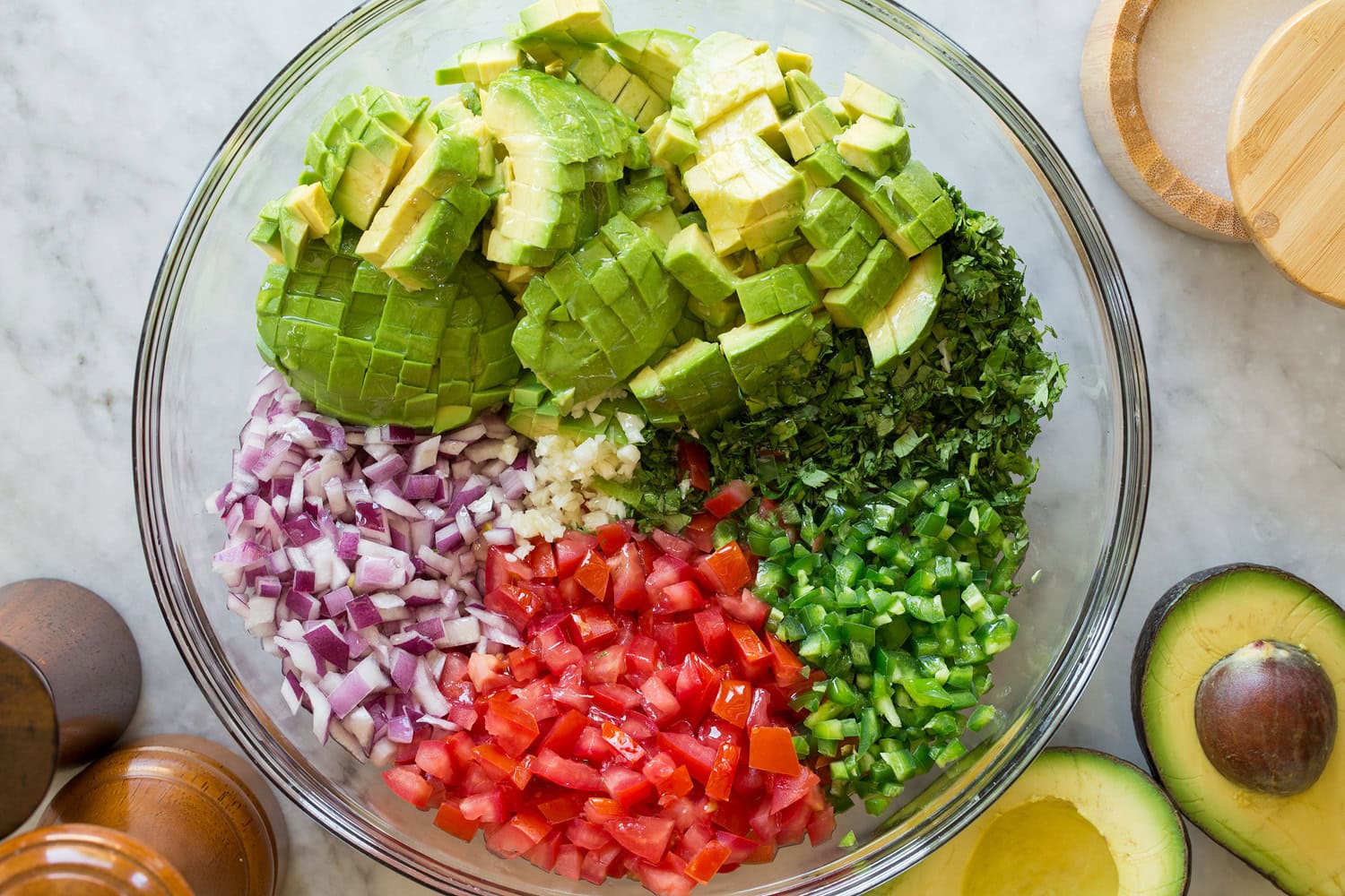 Whole avocados, limes, cilantro, red onion, and a can of chipotle in adobo arranged on a clean kitchen counter under soft daylight