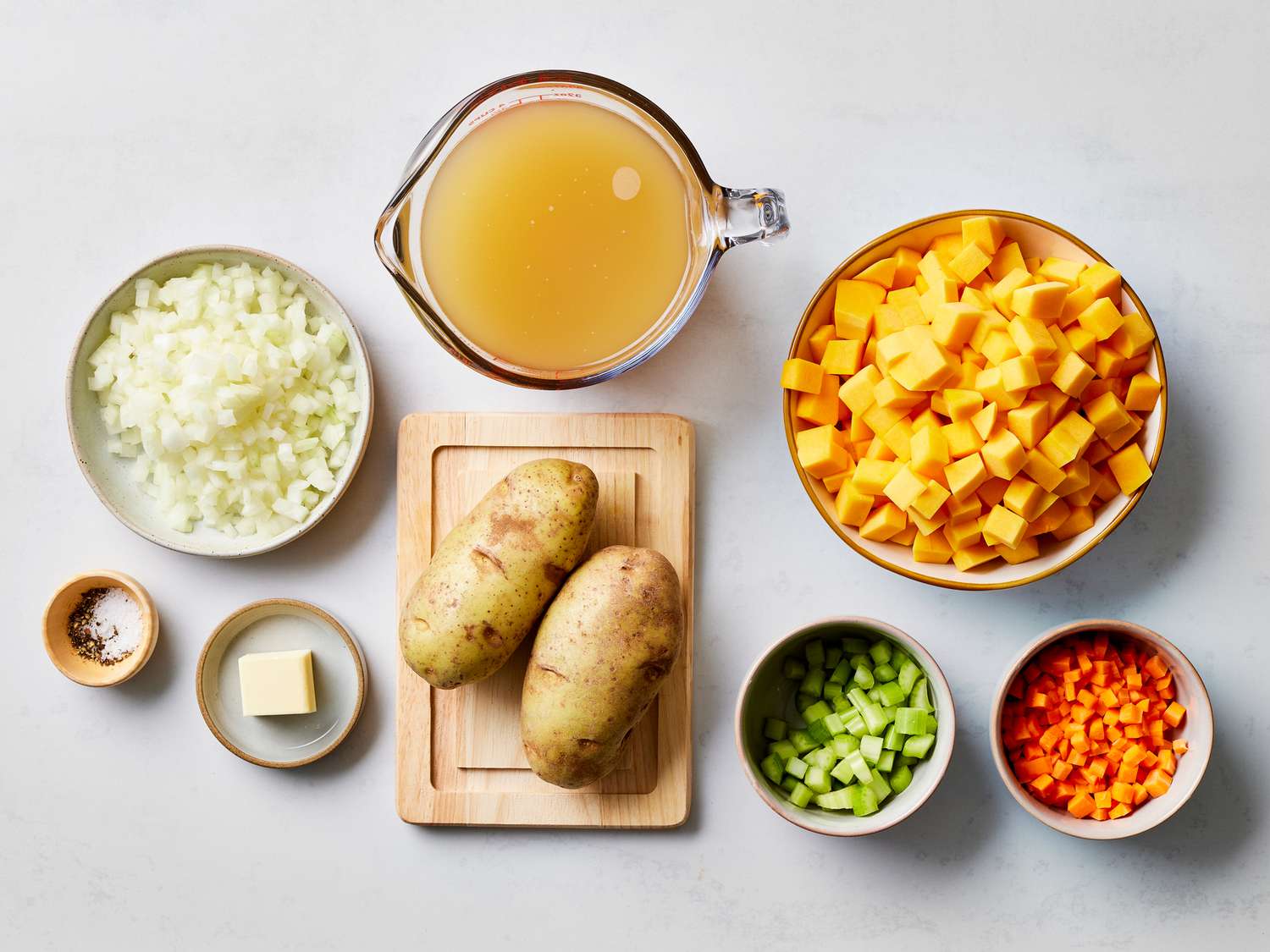 Whole butternut squash, olive oil, kosher salt, black pepper, garlic powder, and fresh rosemary arranged on a clean wooden cutting board on a bright kitchen counter