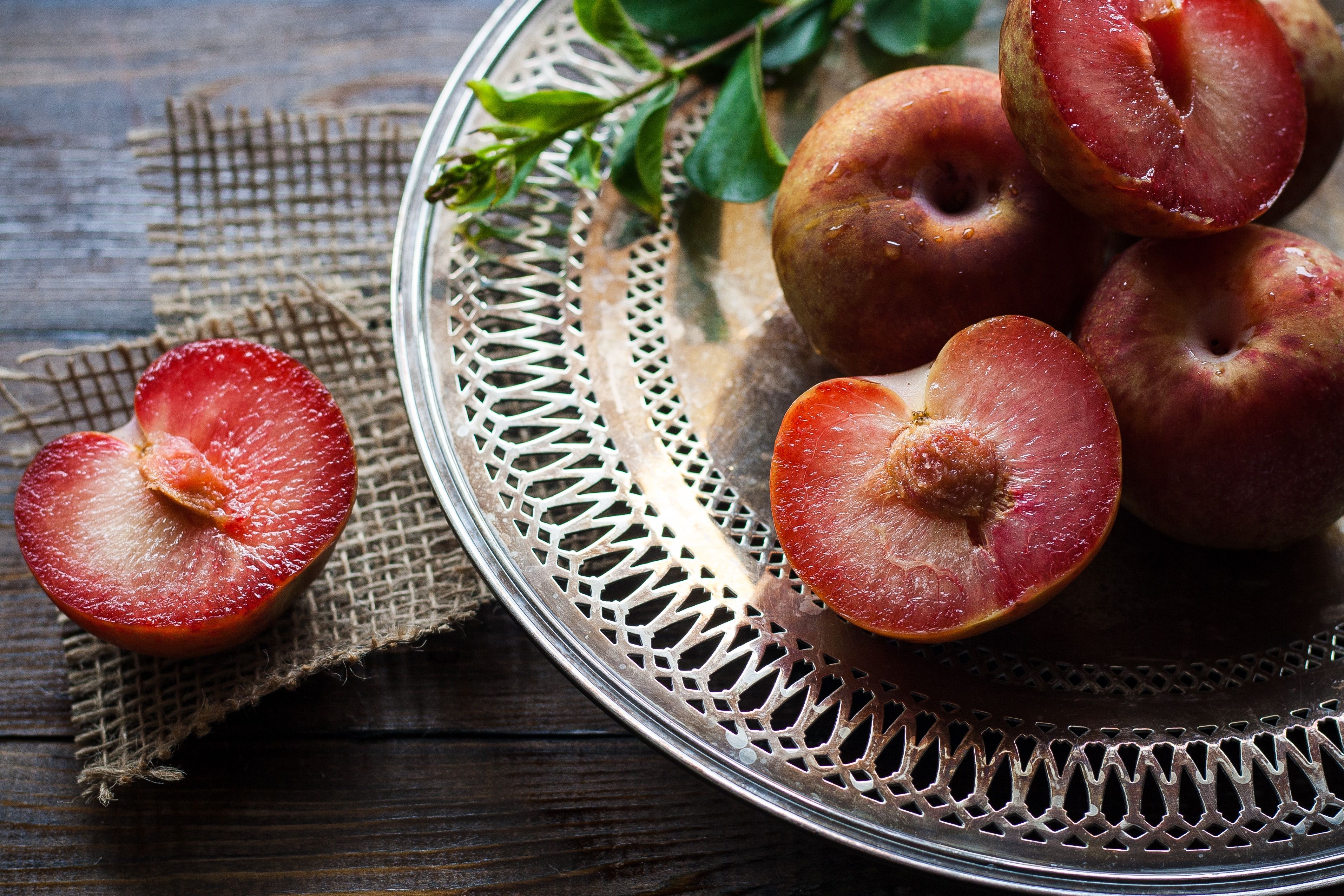 Whole fresh plums piled on a wooden cutting board on a home kitchen counter, with a paring knife nearby