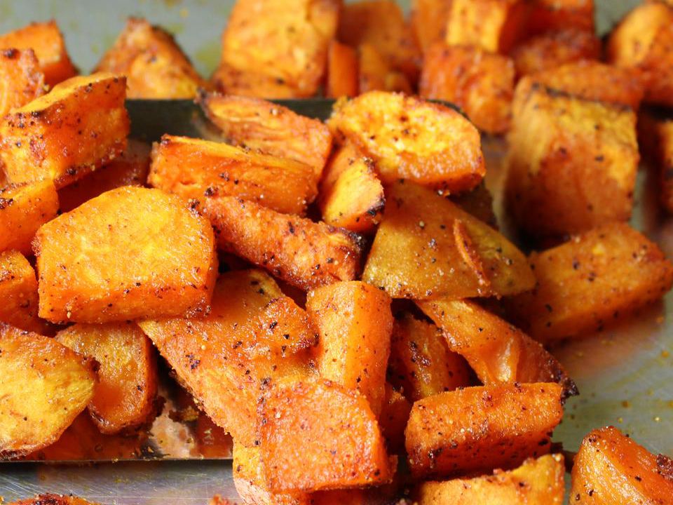 Whole kumara (sweet potatoes) next to small bowls of cornstarch, smoked paprika, garlic powder, salt, pepper, and olive oil on a clean kitchen counter